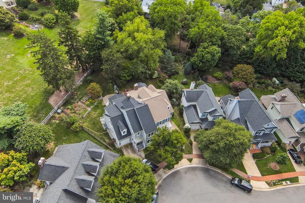 Aerial view of a gray multi-gabled house surrounded by trees and neighboring homes on a cul-de-sac.