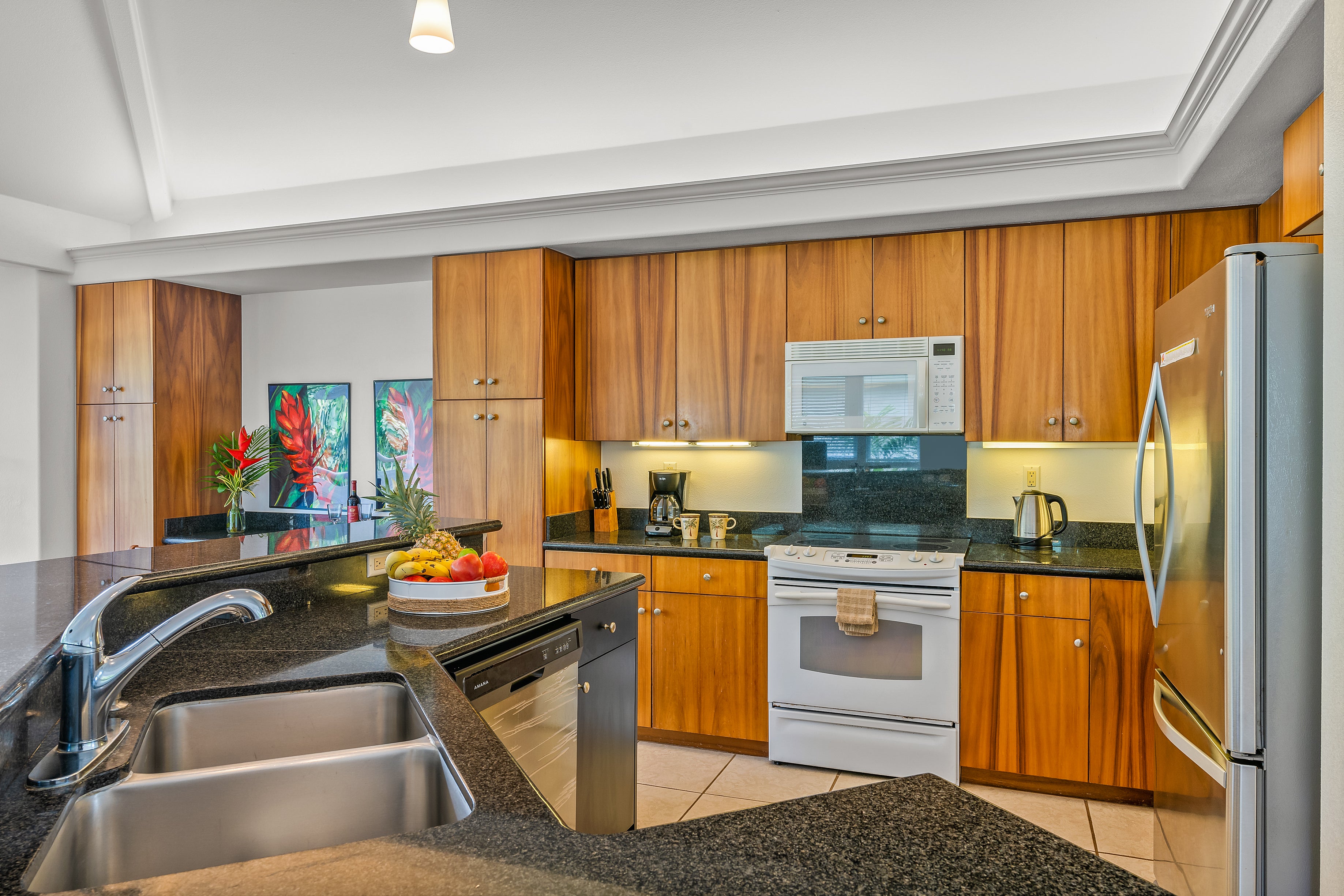 Kitchen with warm wood cabinets, black granite counters, a double sink, and white range.