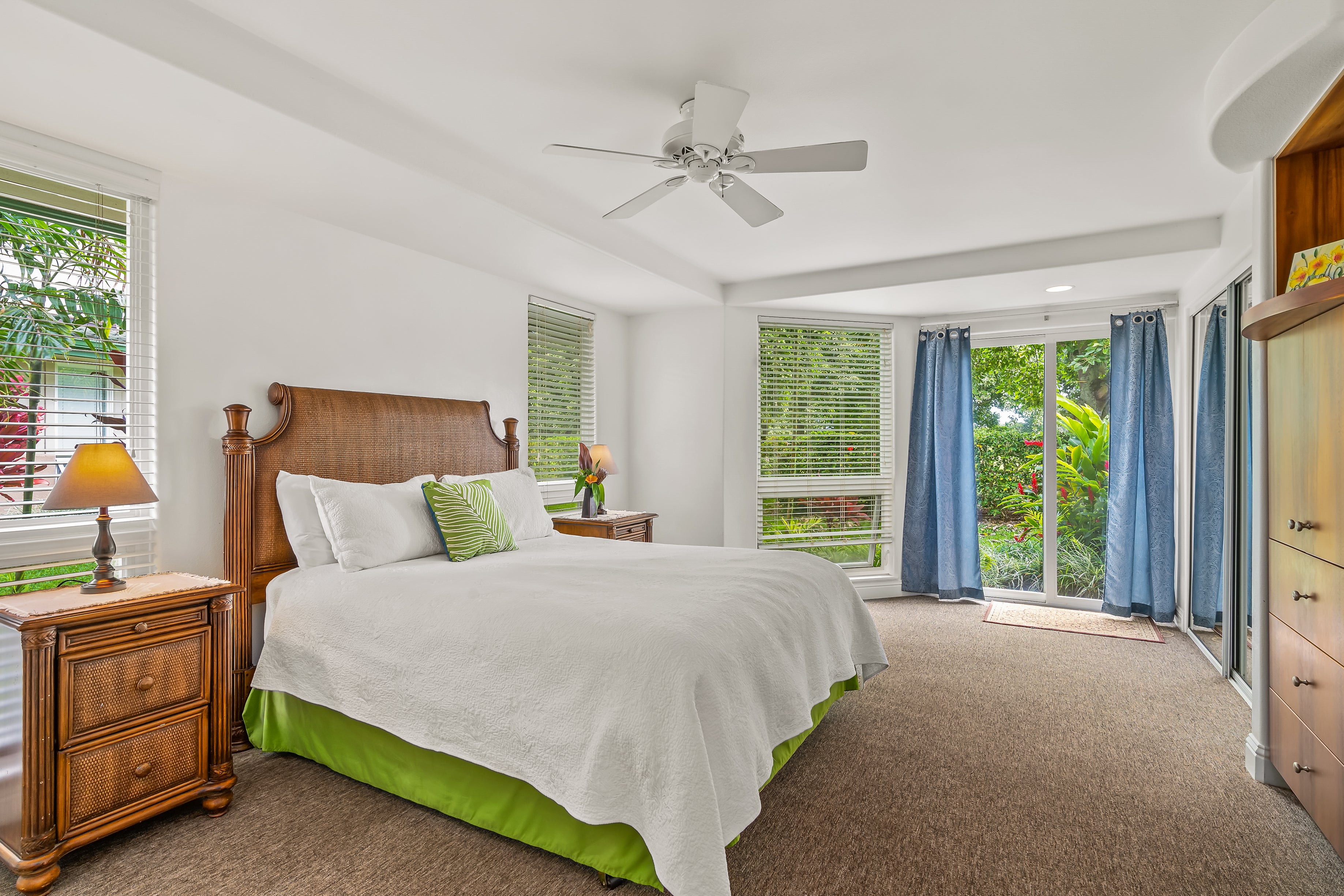 Bright bedroom with a large bed, carved wooden furnishings, and sliding doors opening to tropical greenery.