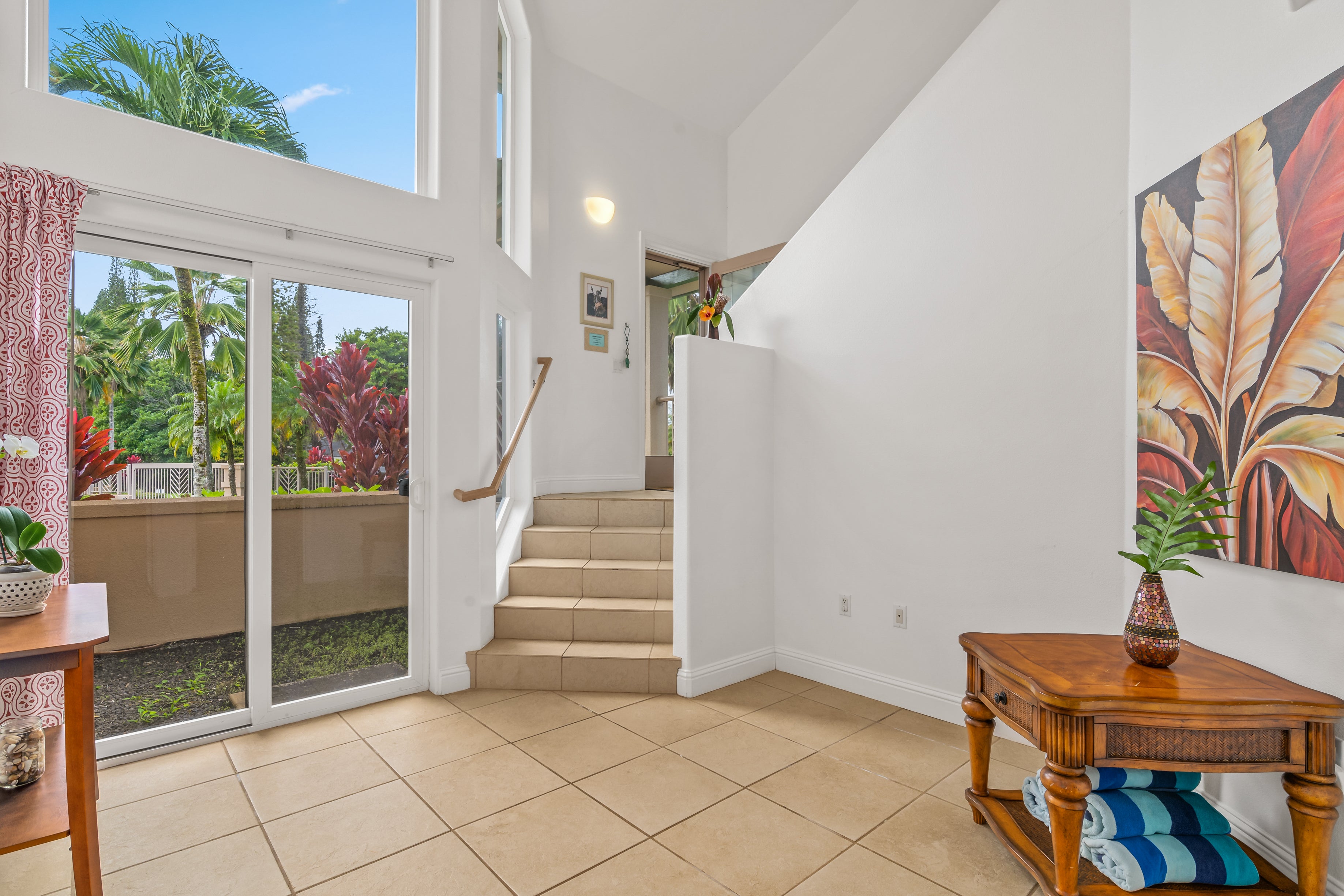 Bright tiled entryway with stairs and tall windows overlooking tropical greenery.