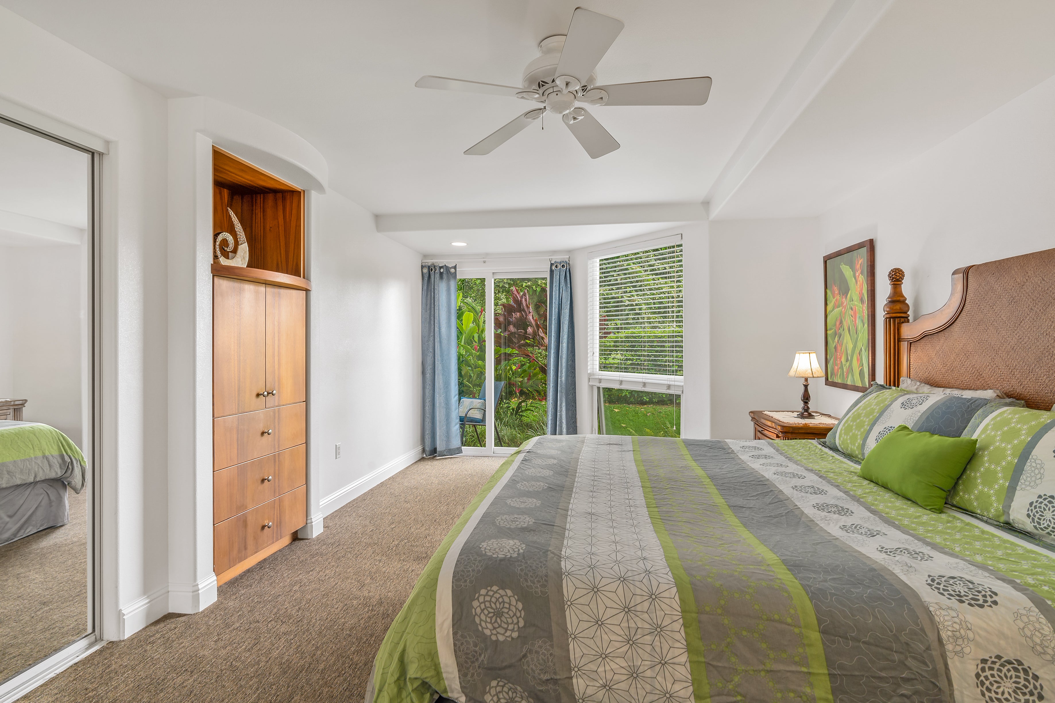 Bedroom with gray and green bedding, built-in wood cabinetry, and sliding doors overlooking a lush garden.