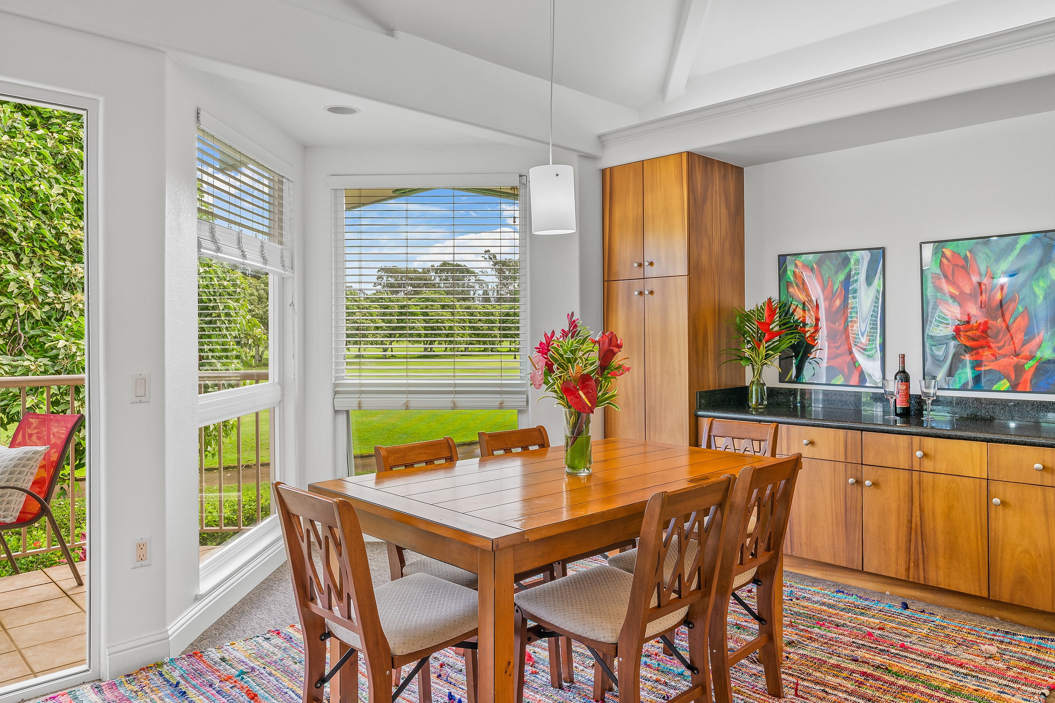 Dining room with a wooden table, colorful rug, built-in cabinetry, and windows overlooking greenery.