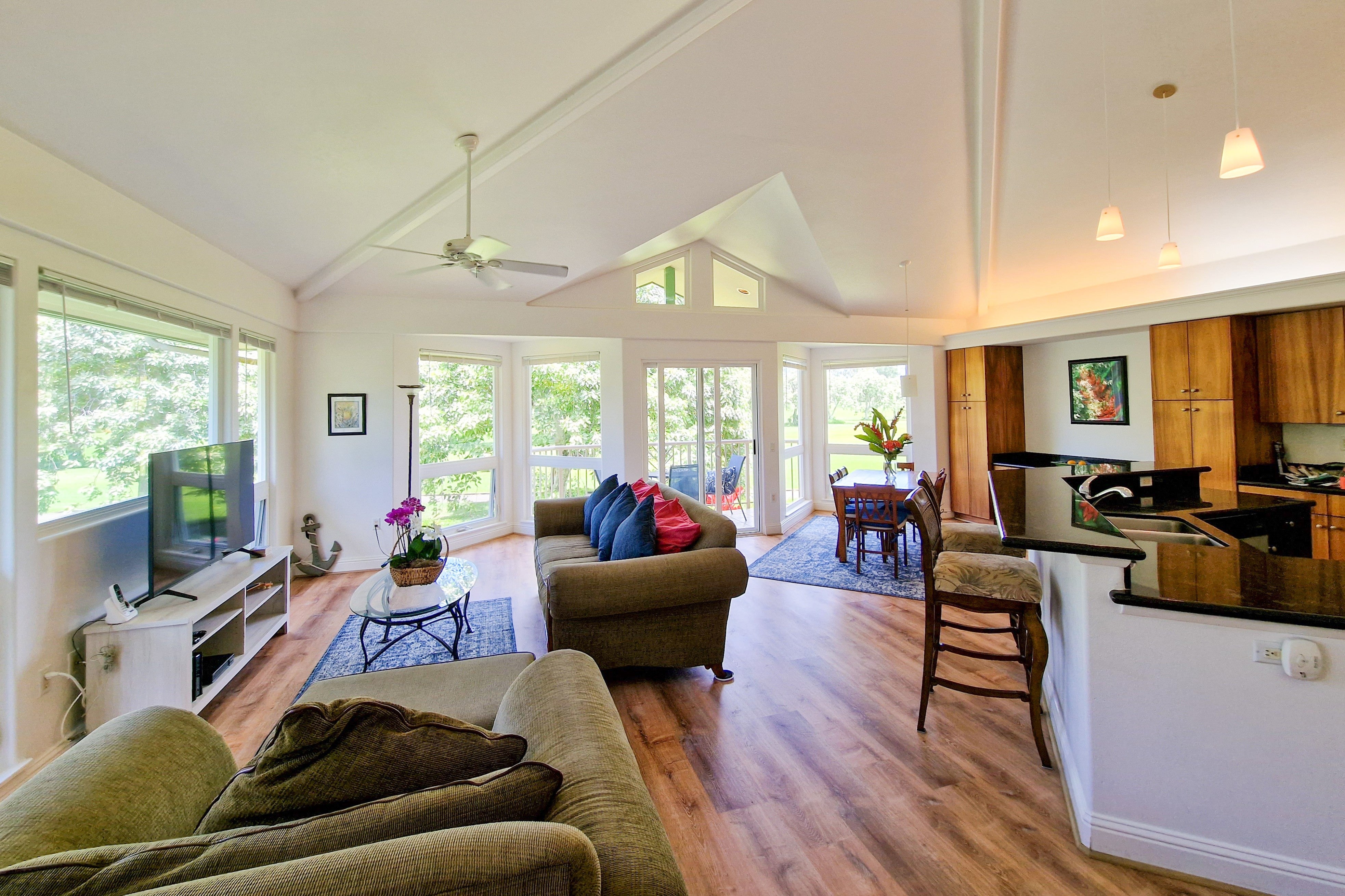 Open-plan living room with vaulted ceiling, large windows, and an adjoining kitchen with island.