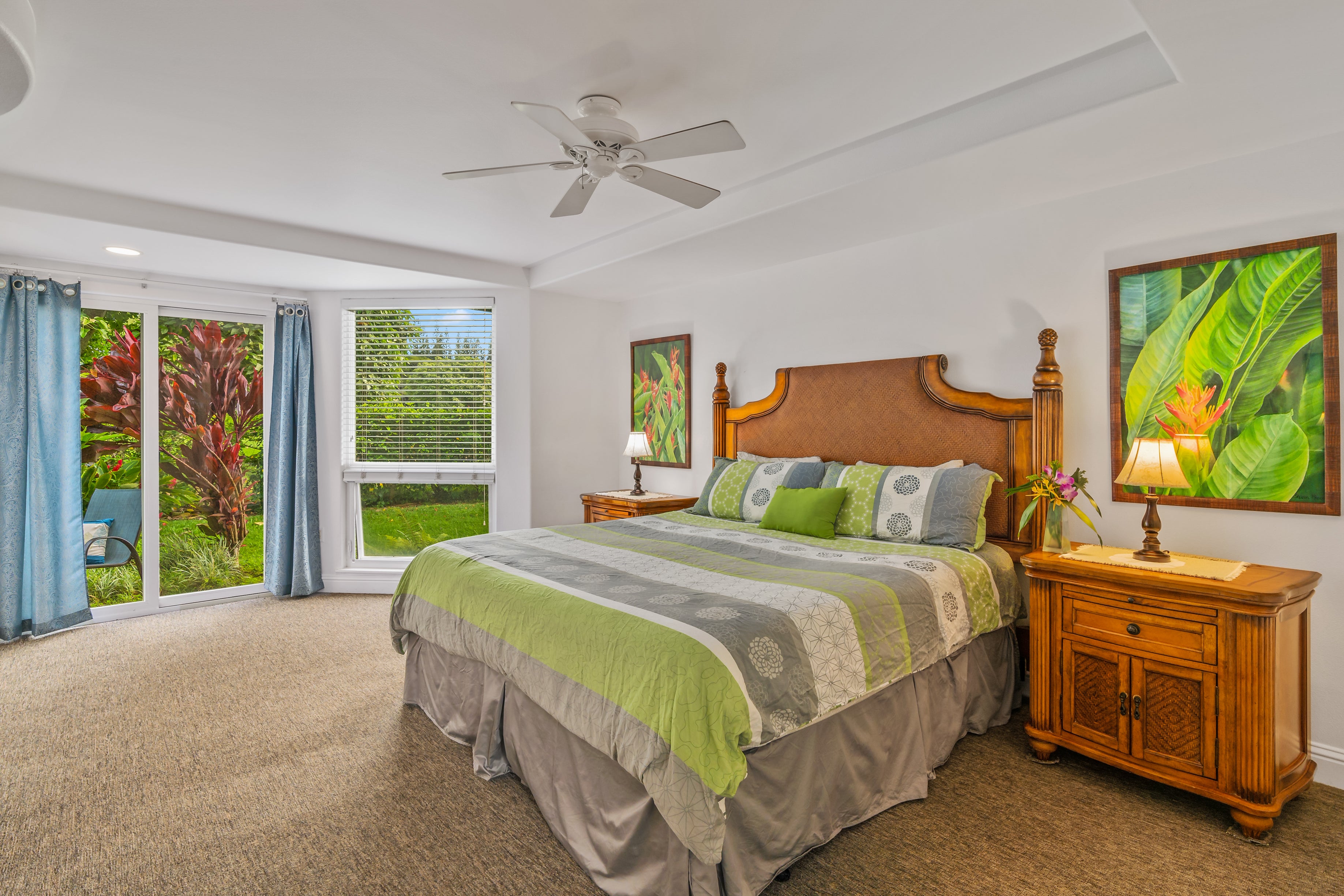 Furnished bedroom with green-and-gray bedding, a carved wood headboard, and garden-facing glass doors.