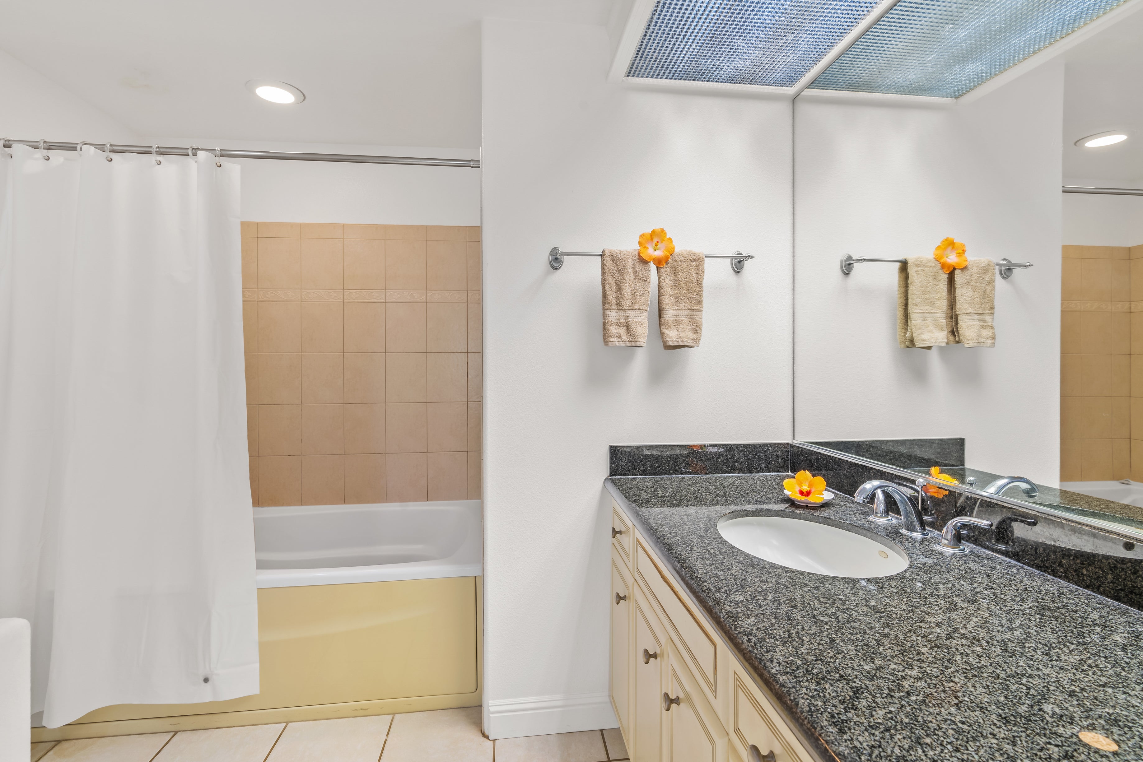 Bathroom with a granite vanity, large mirror, and curtained bathtub with tan tile.