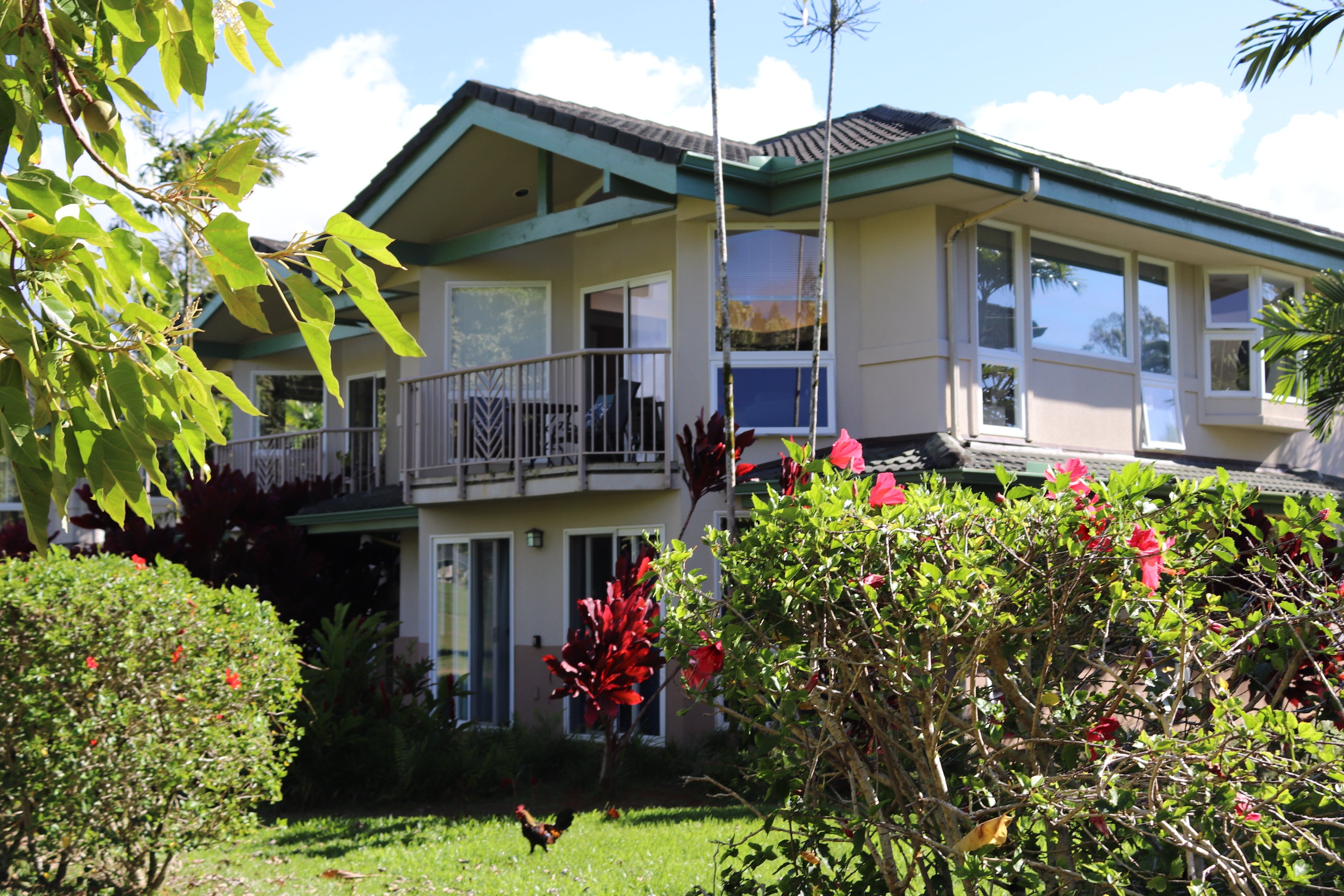 Two-story home with a balcony and tropical flowering shrubs in the foreground.