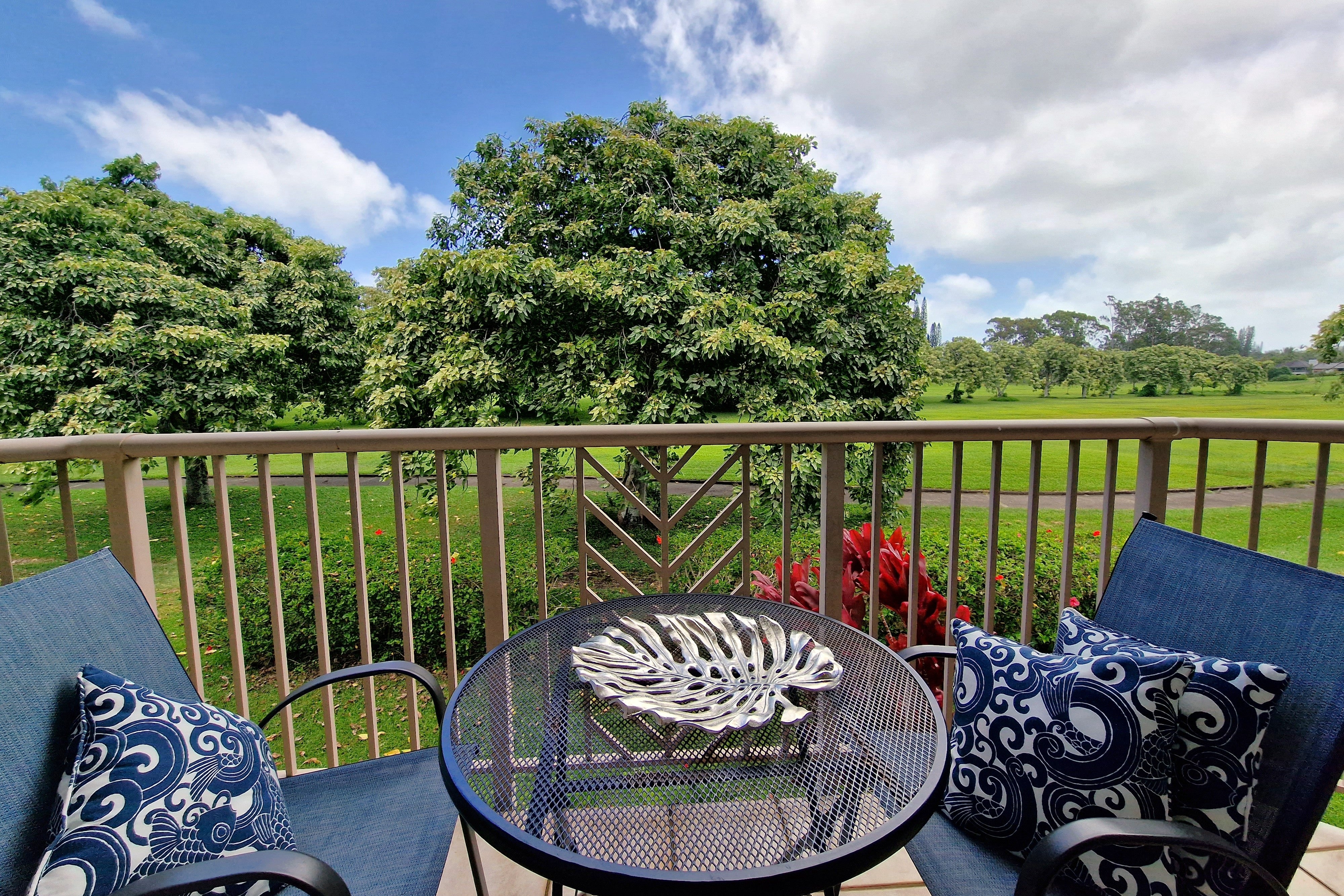 Furnished patio overlooking a manicured lawn and leafy trees, with blue chairs and a round metal table.