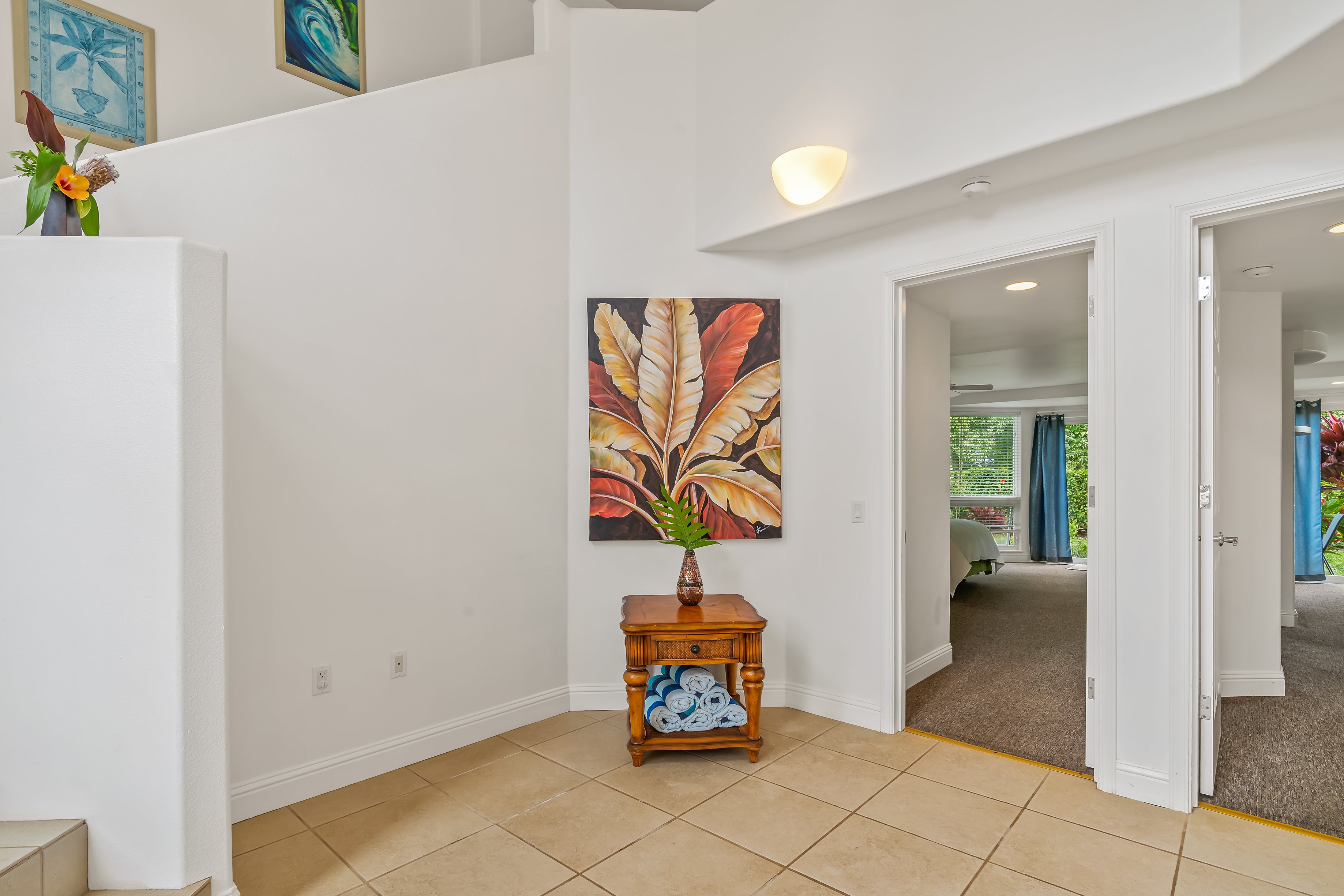 Tiled entry hall with tropical leaf artwork and a wooden console table between bedroom doorways.