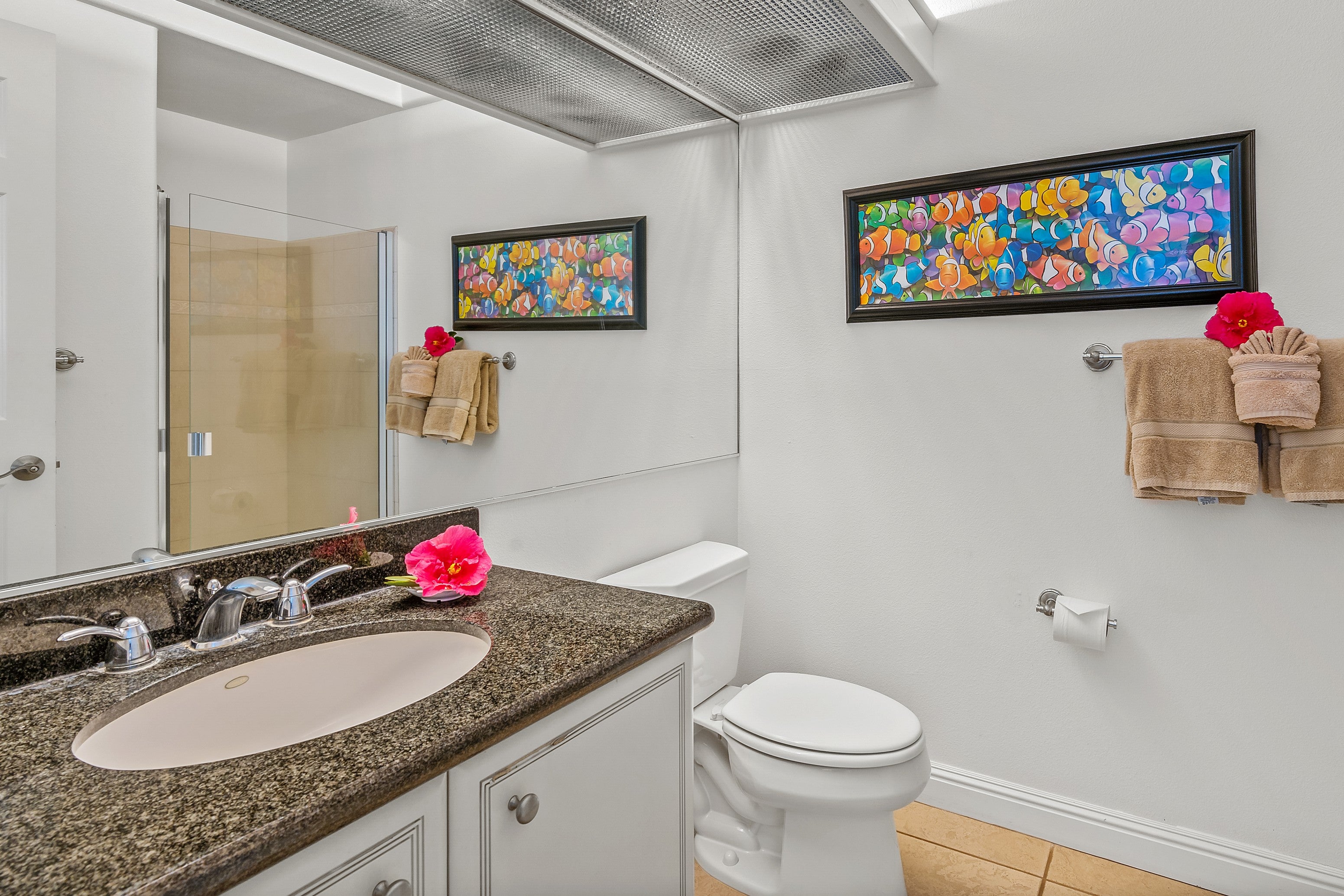 Bathroom with a granite vanity, glass shower, and colorful fish artwork on the walls.
