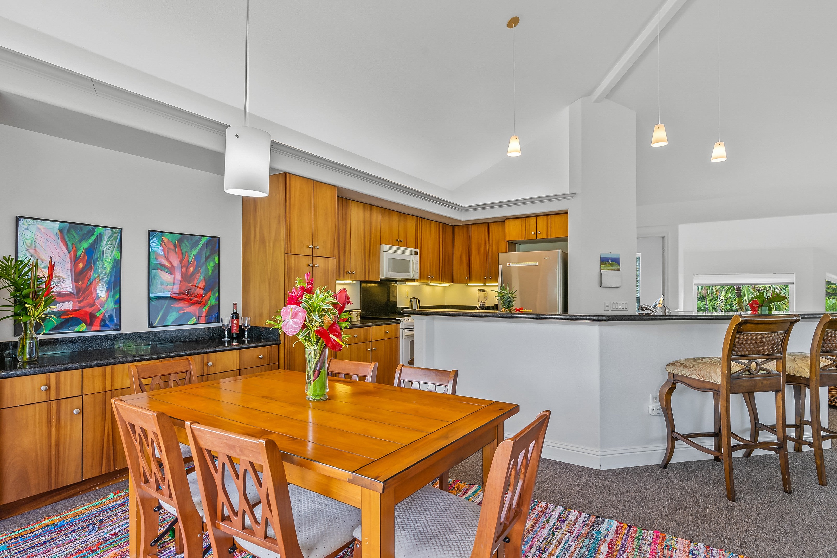 Open-plan kitchen and dining area with warm wood cabinets, a breakfast bar, and a flower centerpiece.