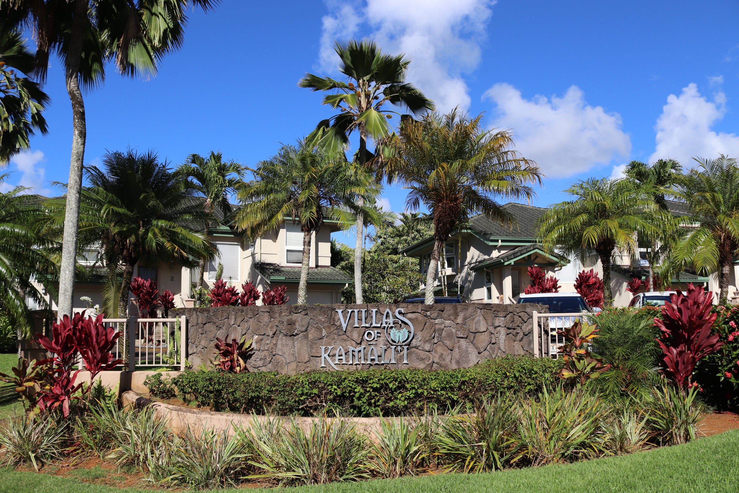 Villas of Kamalii entrance sign amid tropical landscaping, with villa-style homes behind it.