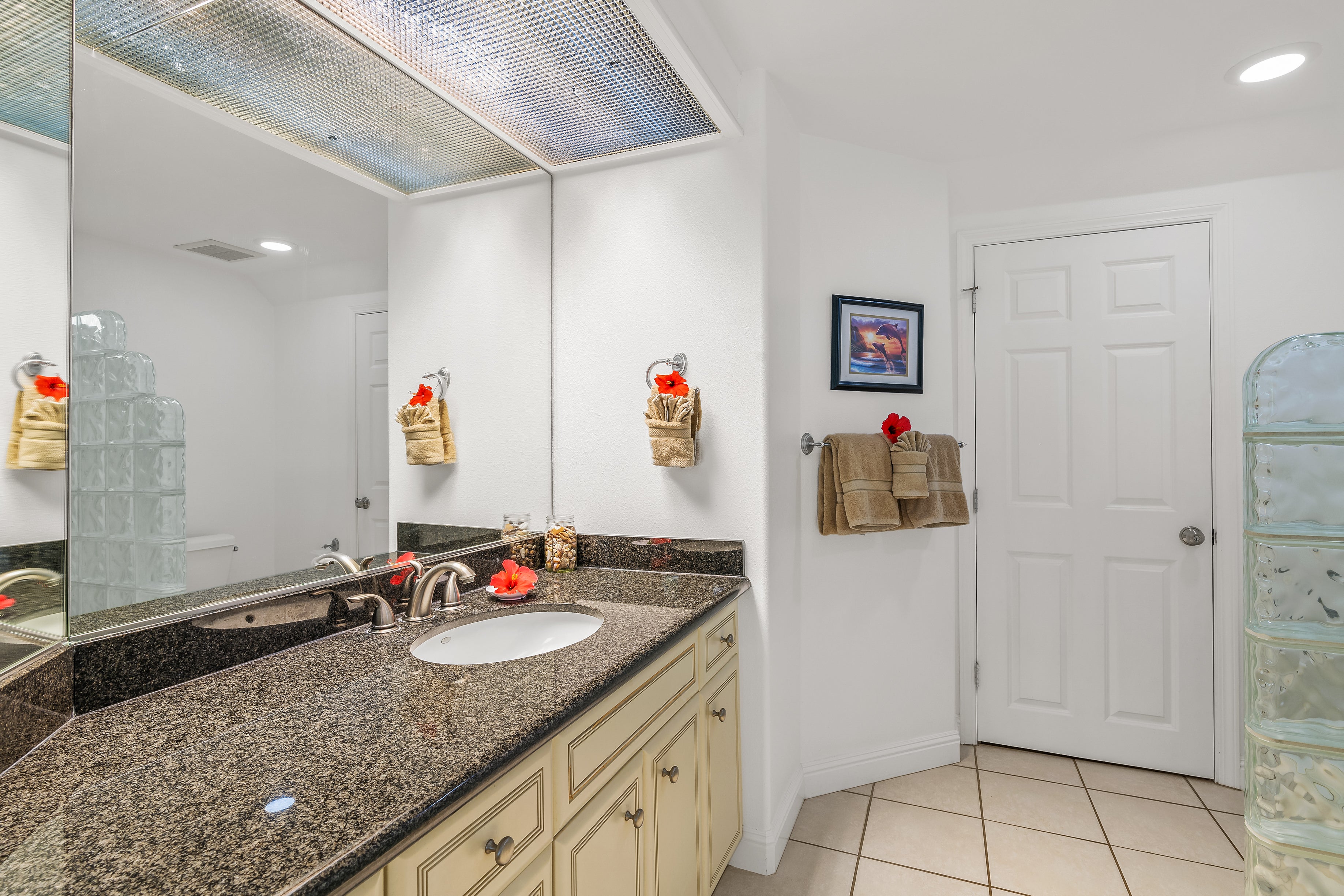Bathroom with a granite vanity, cream cabinets, large mirror, and glass-block accents.