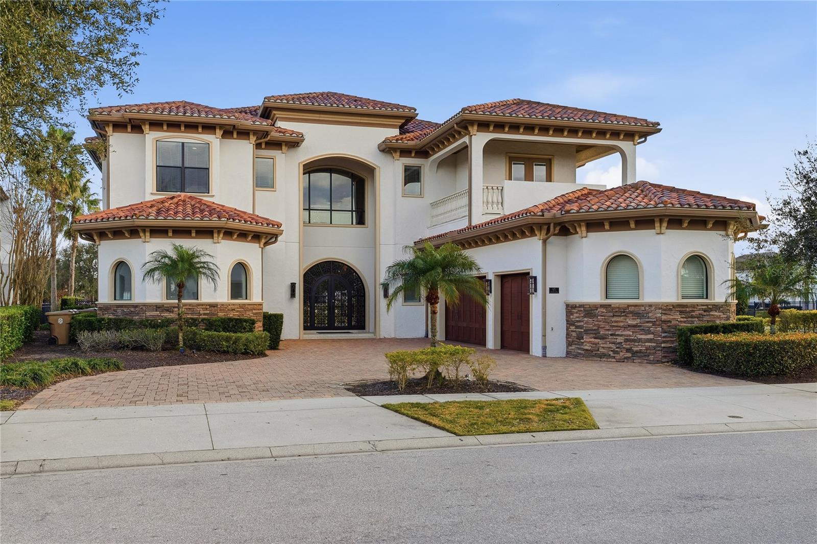 Two-story stucco home with terracotta tile roofs, arched windows, stone accents, and a paved driveway.