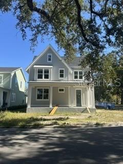 Blue-gray two-story house with white trim and a covered porch beneath mature trees.