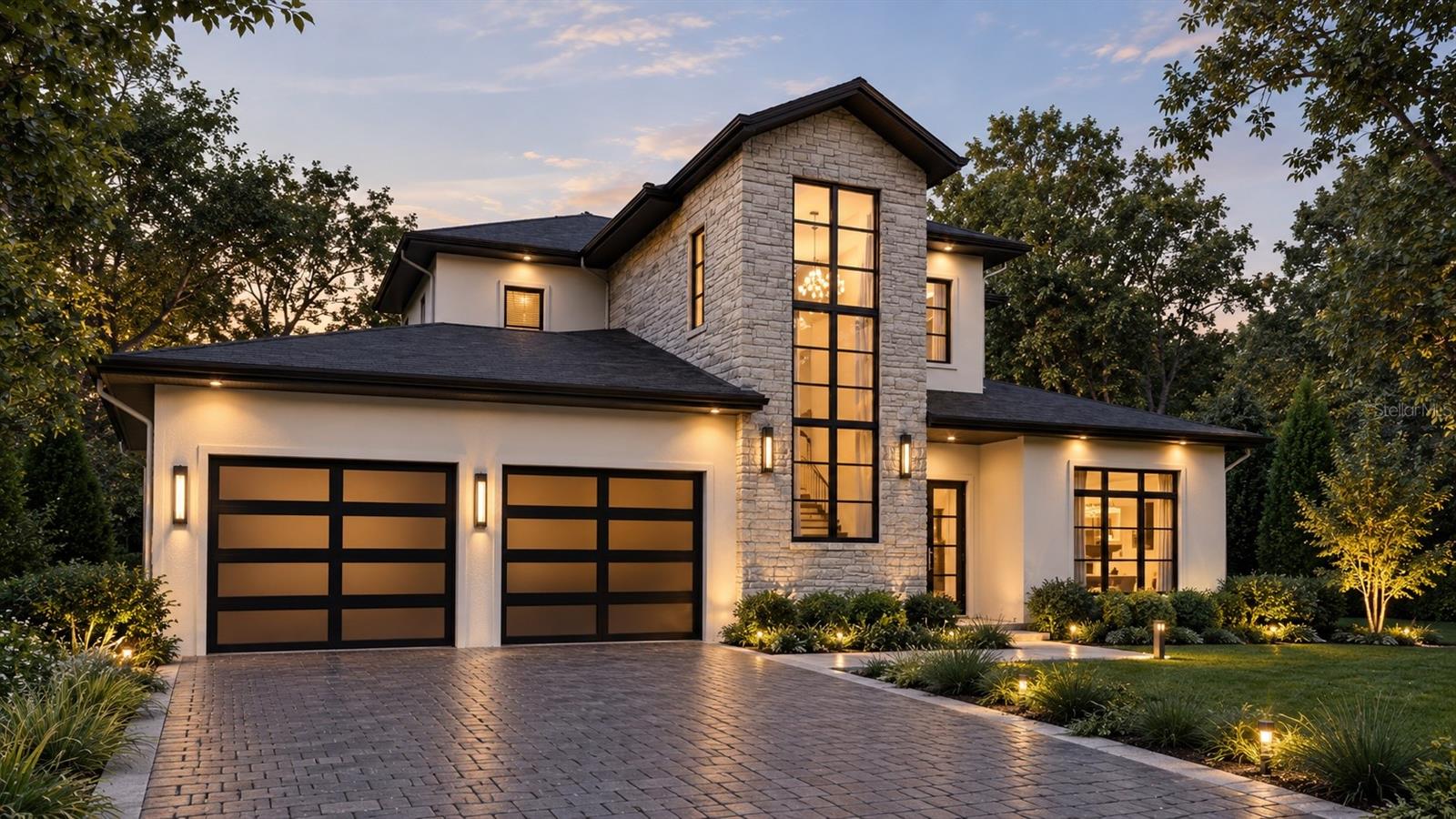 Modern two-story home with a stone tower, illuminated windows, and a broad paved driveway at dusk.