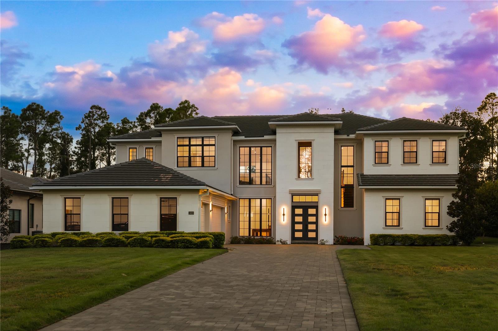 Two-story white home with black-framed windows and a broad paved driveway at dusk.
