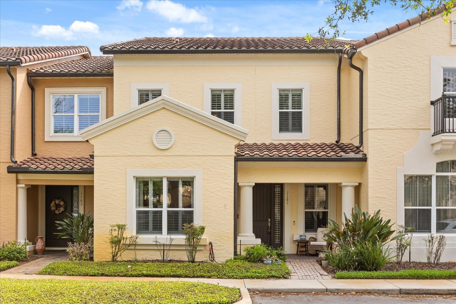Two-story cream stucco townhomes with tiled roofs, covered entrances, and landscaped fronts.