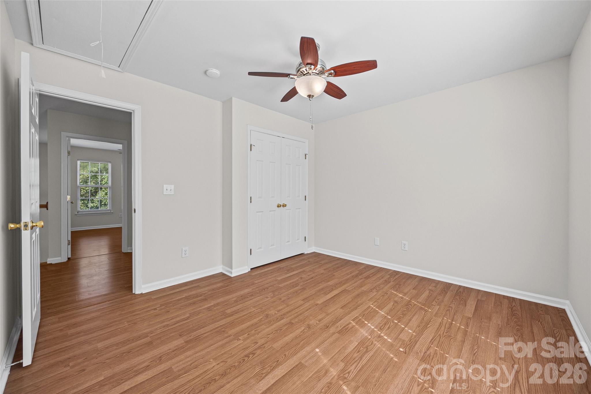 Empty bedroom with hardwood floors, a ceiling fan, and double closet doors.