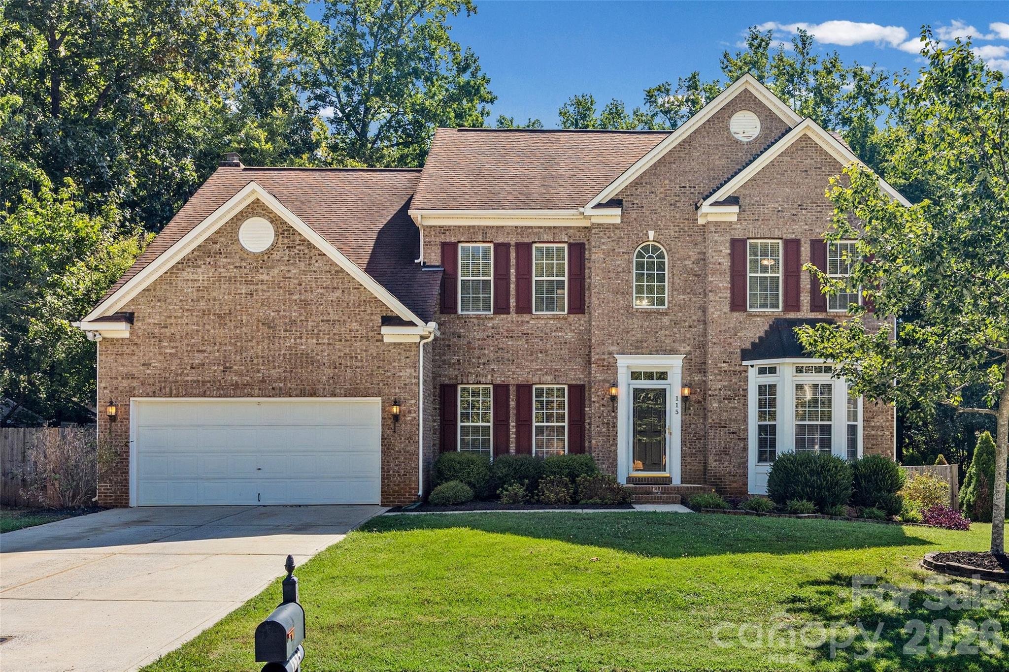 Two-story brick house with burgundy shutters, a double garage, and a green front lawn.