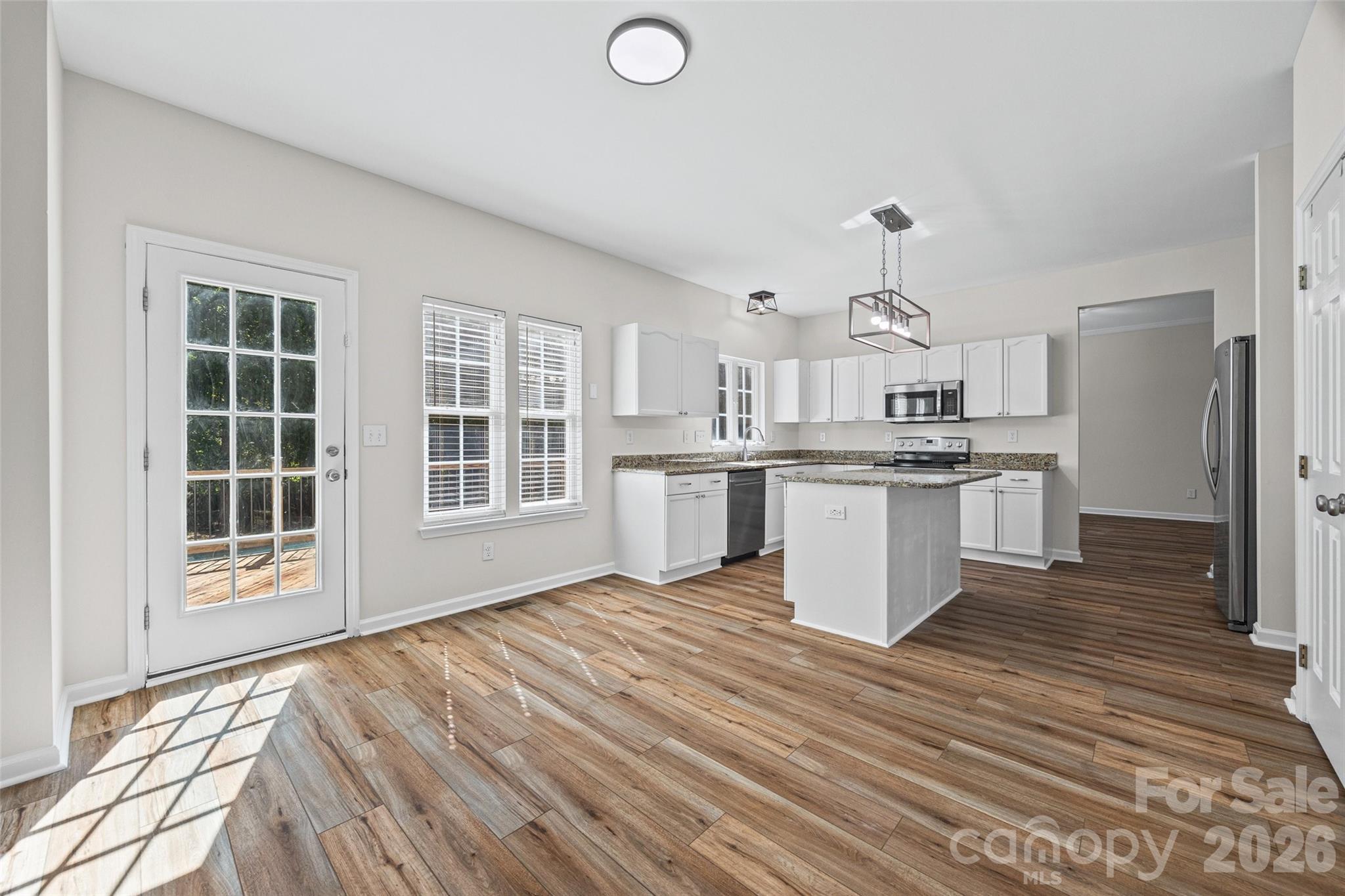 Kitchen with white cabinets, granite counters, a central island, and wood-look flooring.