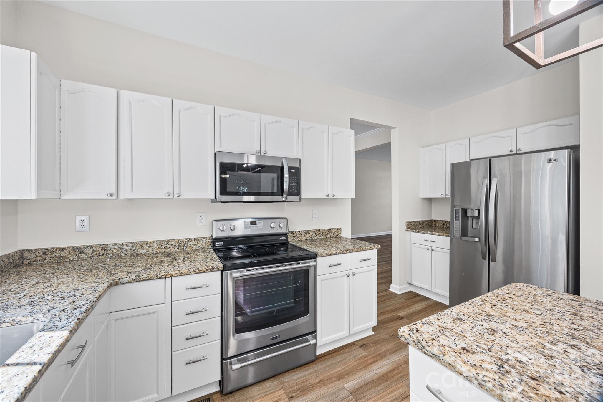 Vacant kitchen with white cabinets, granite counters, stainless steel appliances, and wood-look flooring.