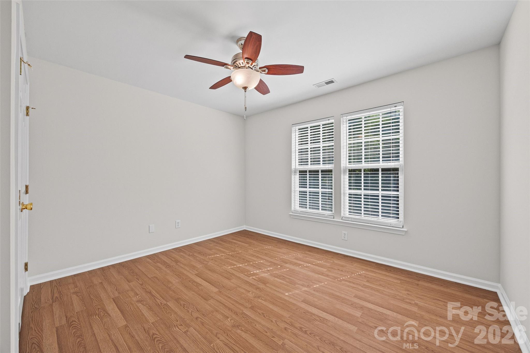 Empty bedroom with wood floors, two blinded windows, and a ceiling fan with light.