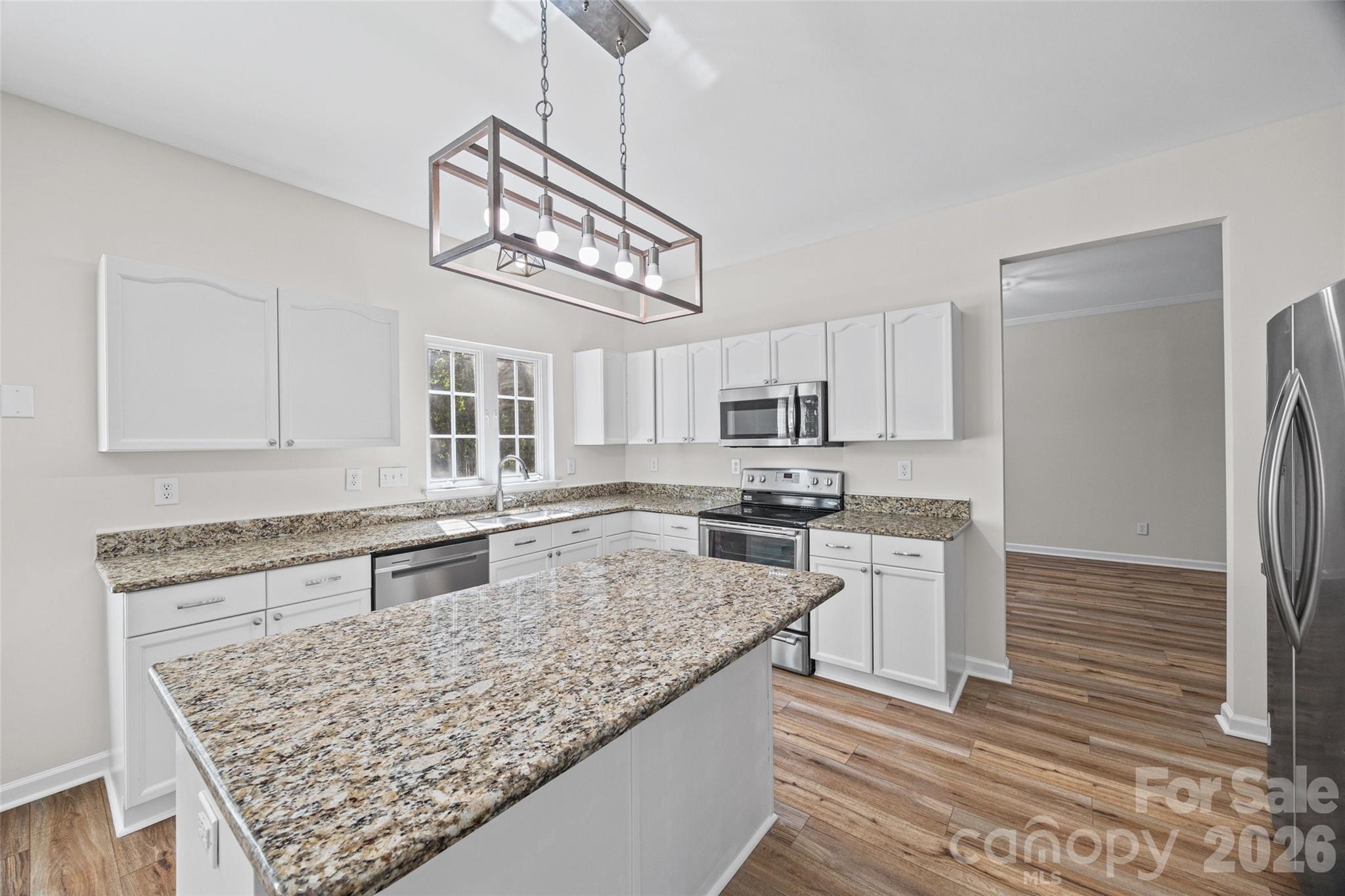 Unfurnished kitchen with white cabinets, granite counters, a large peninsula, and stainless steel appliances.
