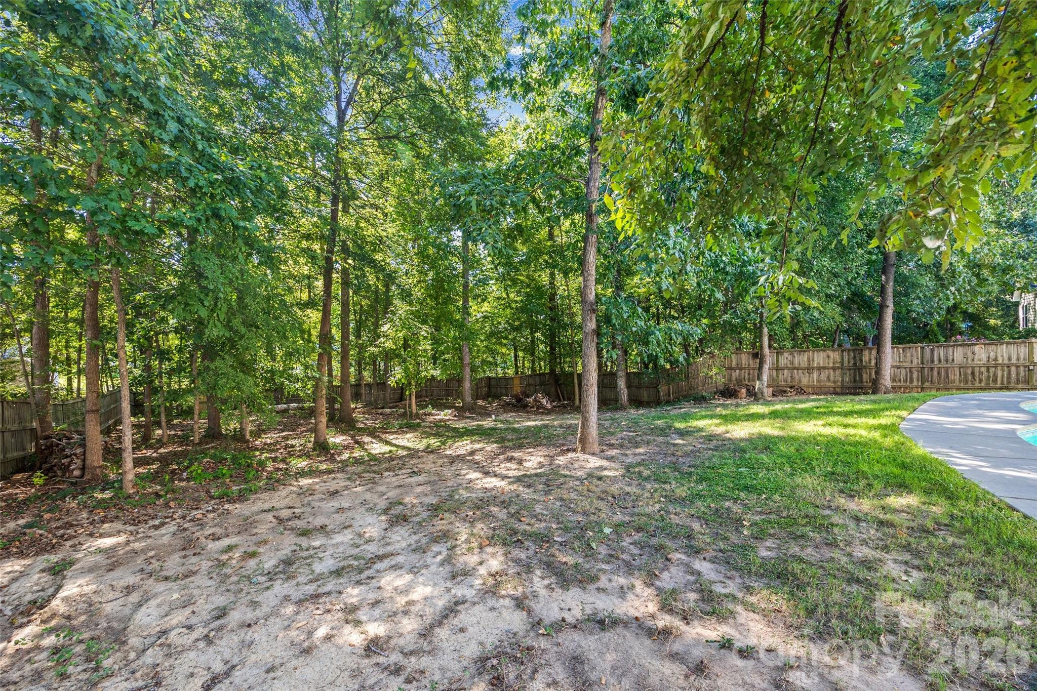 Fenced, tree-shaded backyard with a swimming pool patio along the right edge.