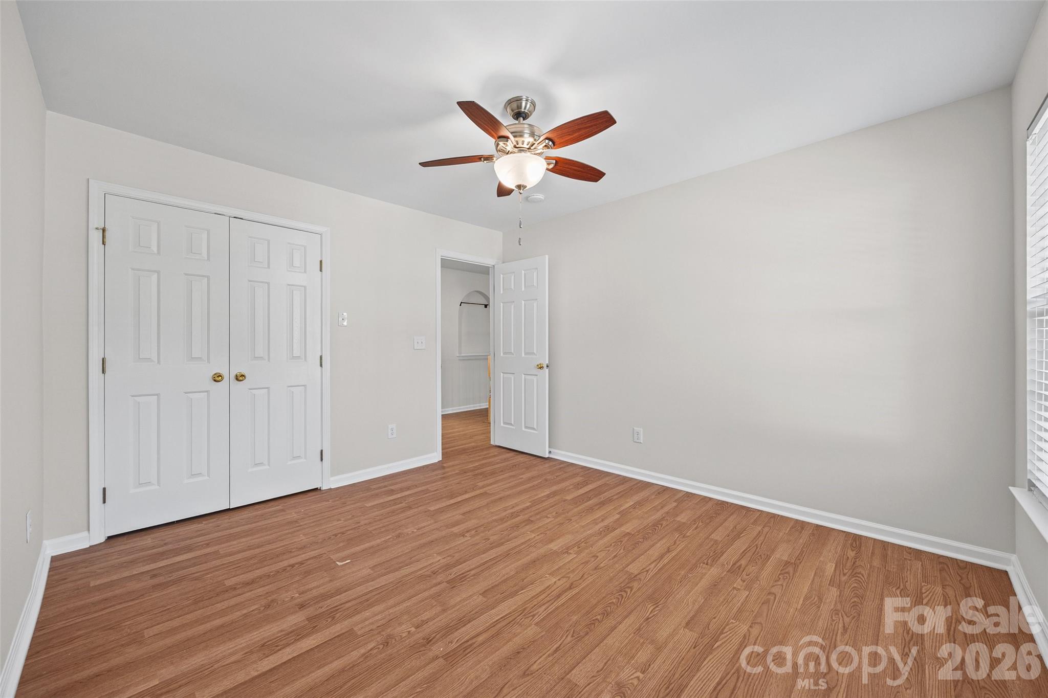 Empty bedroom with hardwood floors, a ceiling fan, and double closet doors.