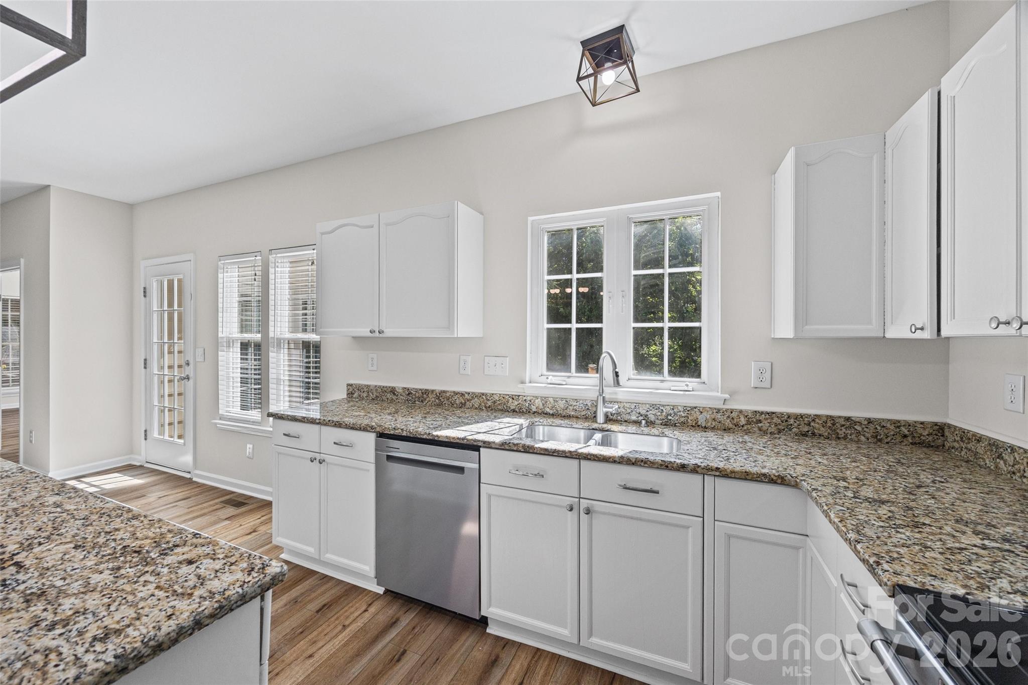 Kitchen with white cabinets, granite countertops, and a double-basin sink beneath a window.