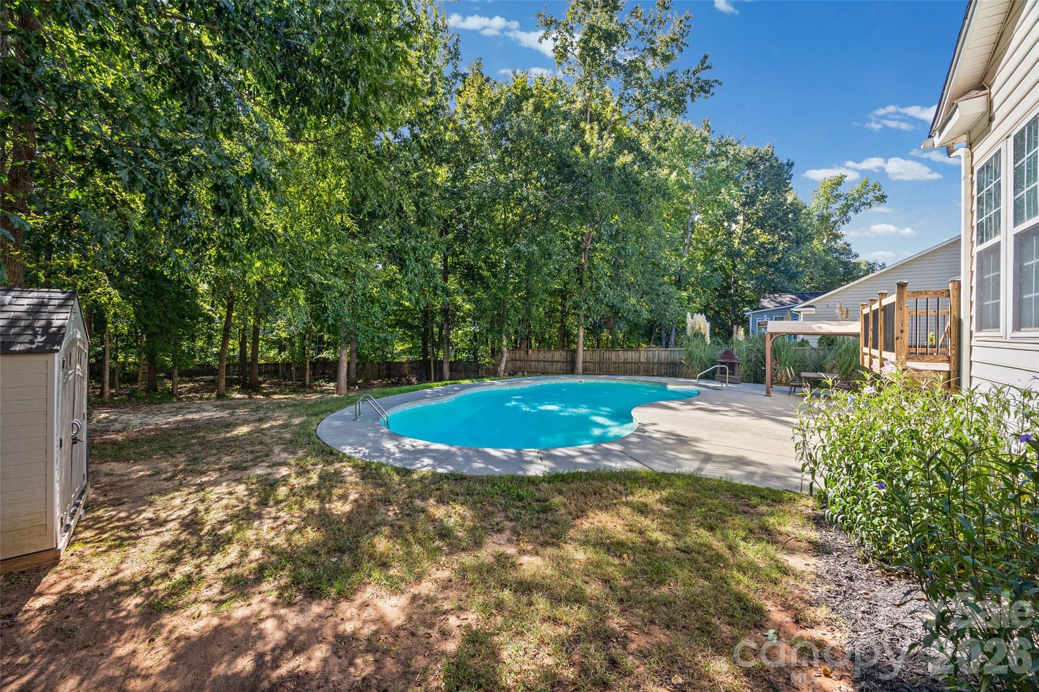 Backyard swimming pool bordered by a concrete patio, wooden deck, and mature trees.