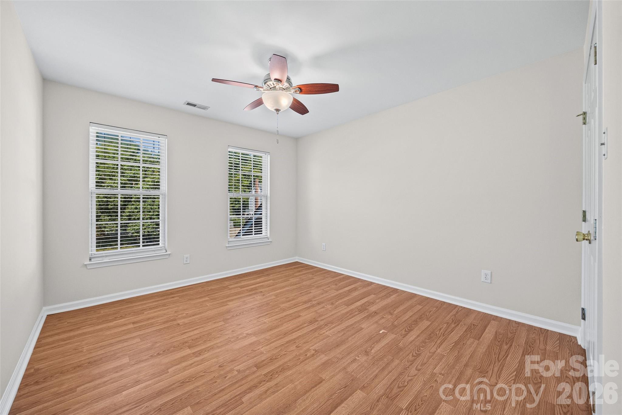 Empty room with wood-look floors, two windows with blinds, and a ceiling fan.