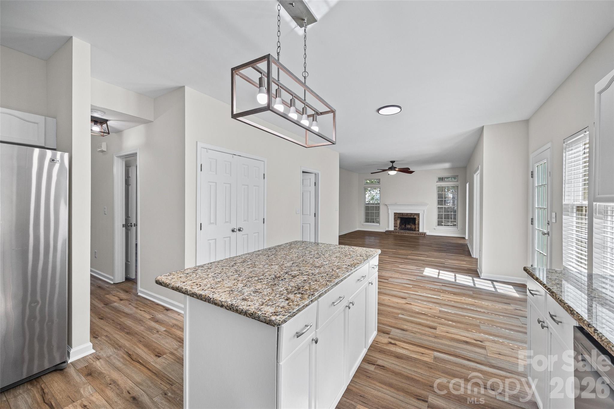 Open kitchen with a large granite island looking toward an unfurnished living room and fireplace.