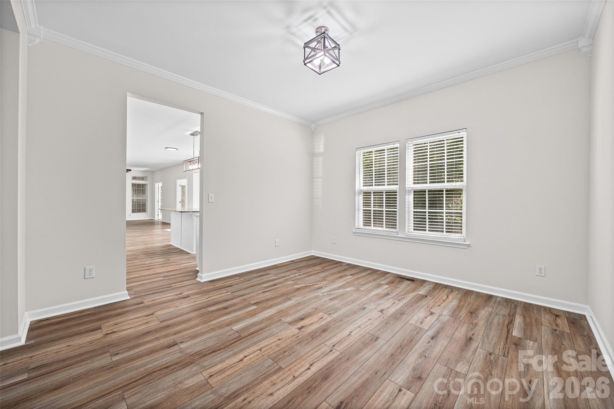 Empty dining area with wood-look floors, two blinded windows, and an opening to the kitchen.