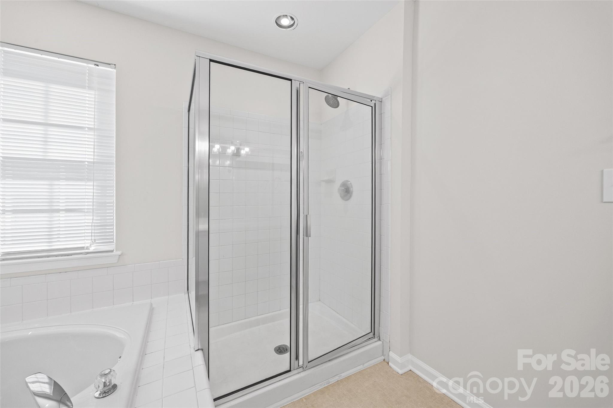 Bathroom with glass-enclosed tiled shower and bathtub beneath a window with white blinds.