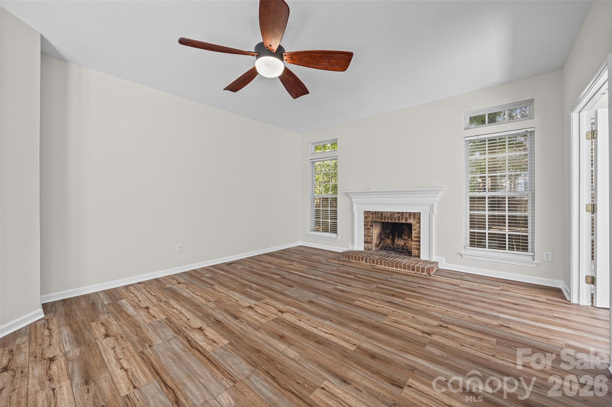 Unfurnished living room with a brick fireplace, wood-look floors, tall windows, and a ceiling fan.