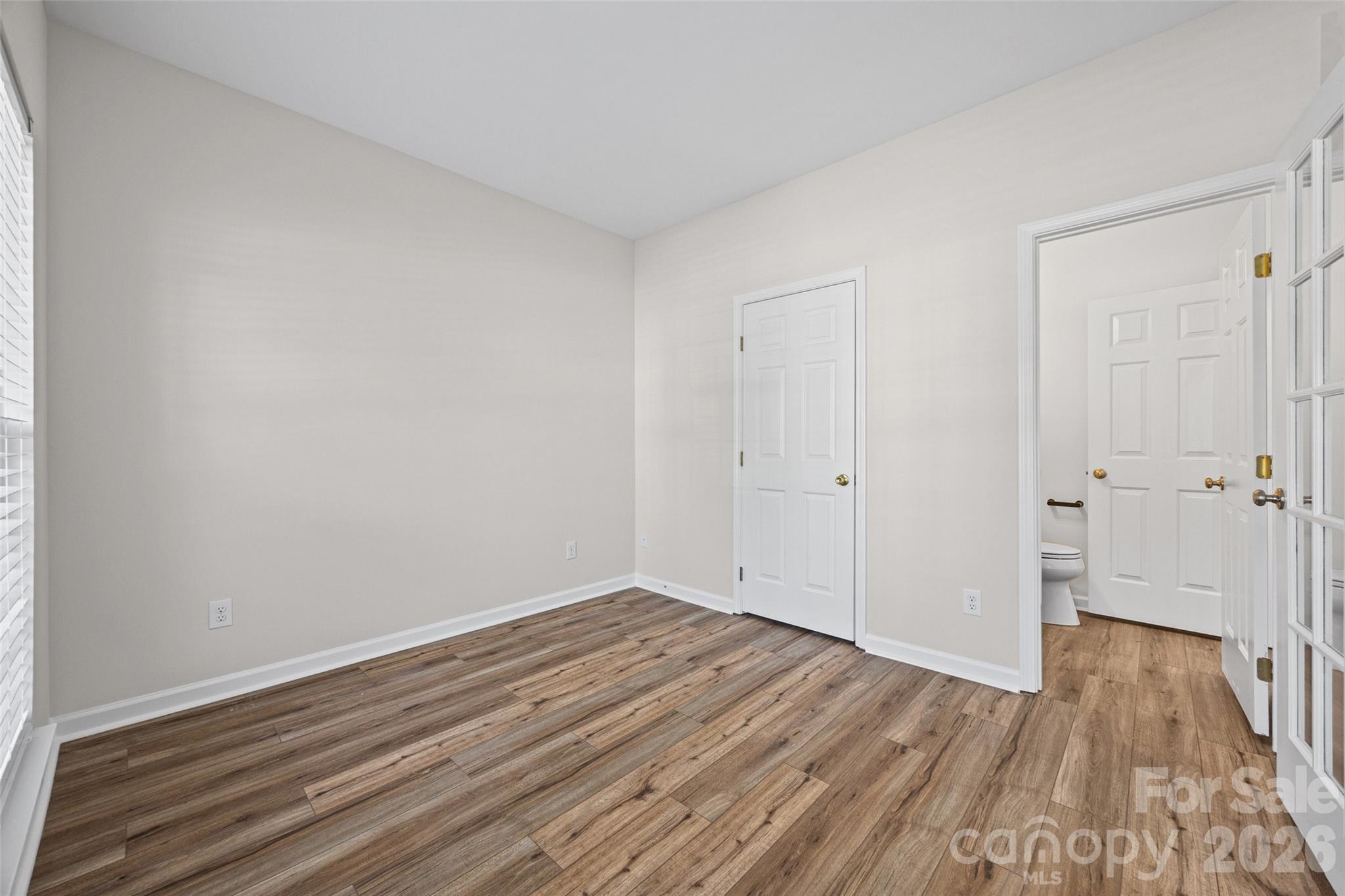 Empty bedroom with wood-look flooring and an open doorway to an adjoining bathroom.