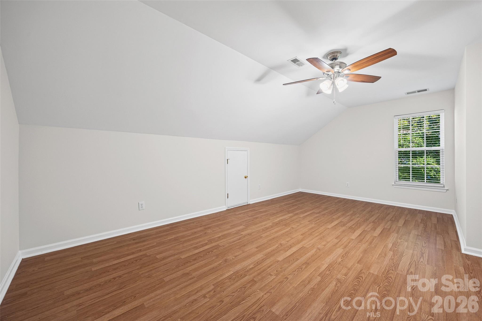 Empty bedroom with warm wood floors, a vaulted ceiling, and a ceiling fan.