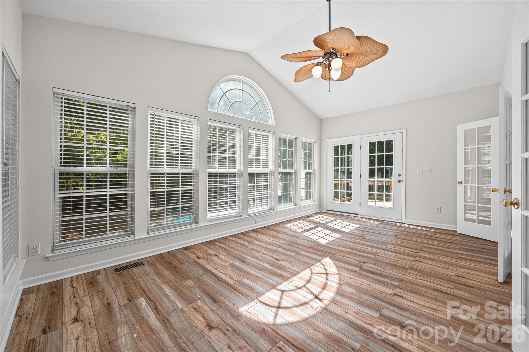 Vacant sunroom with vaulted ceiling, wood-look floors, arched window, and French doors.