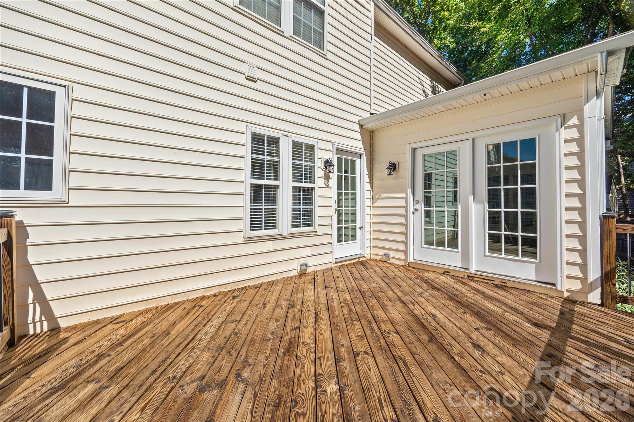 Wooden backyard deck beside a white-sided home, with French doors and a covered entry.