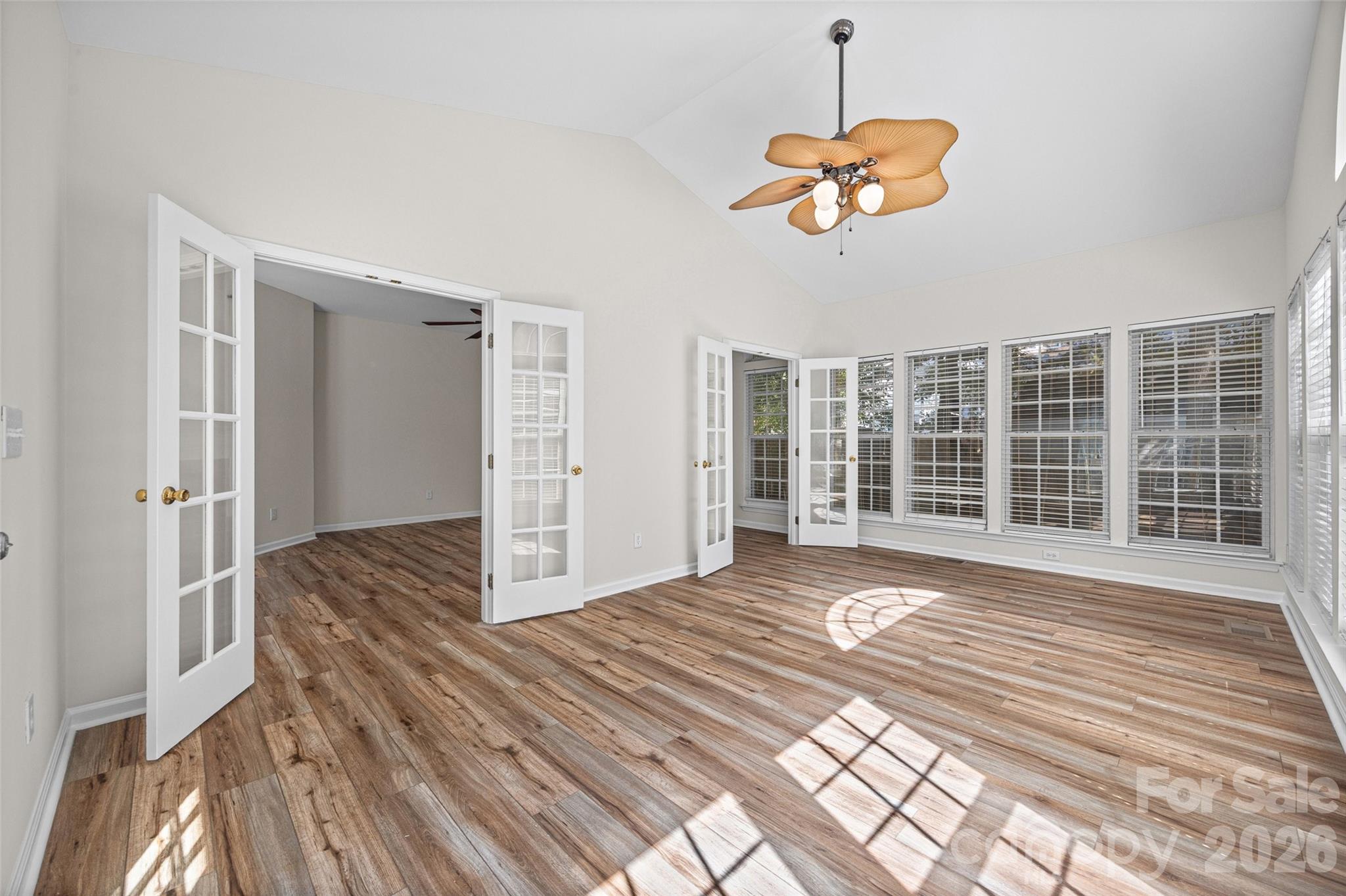 Vacant sunroom with wood-look flooring, vaulted ceiling, ceiling fan, and rows of windows.