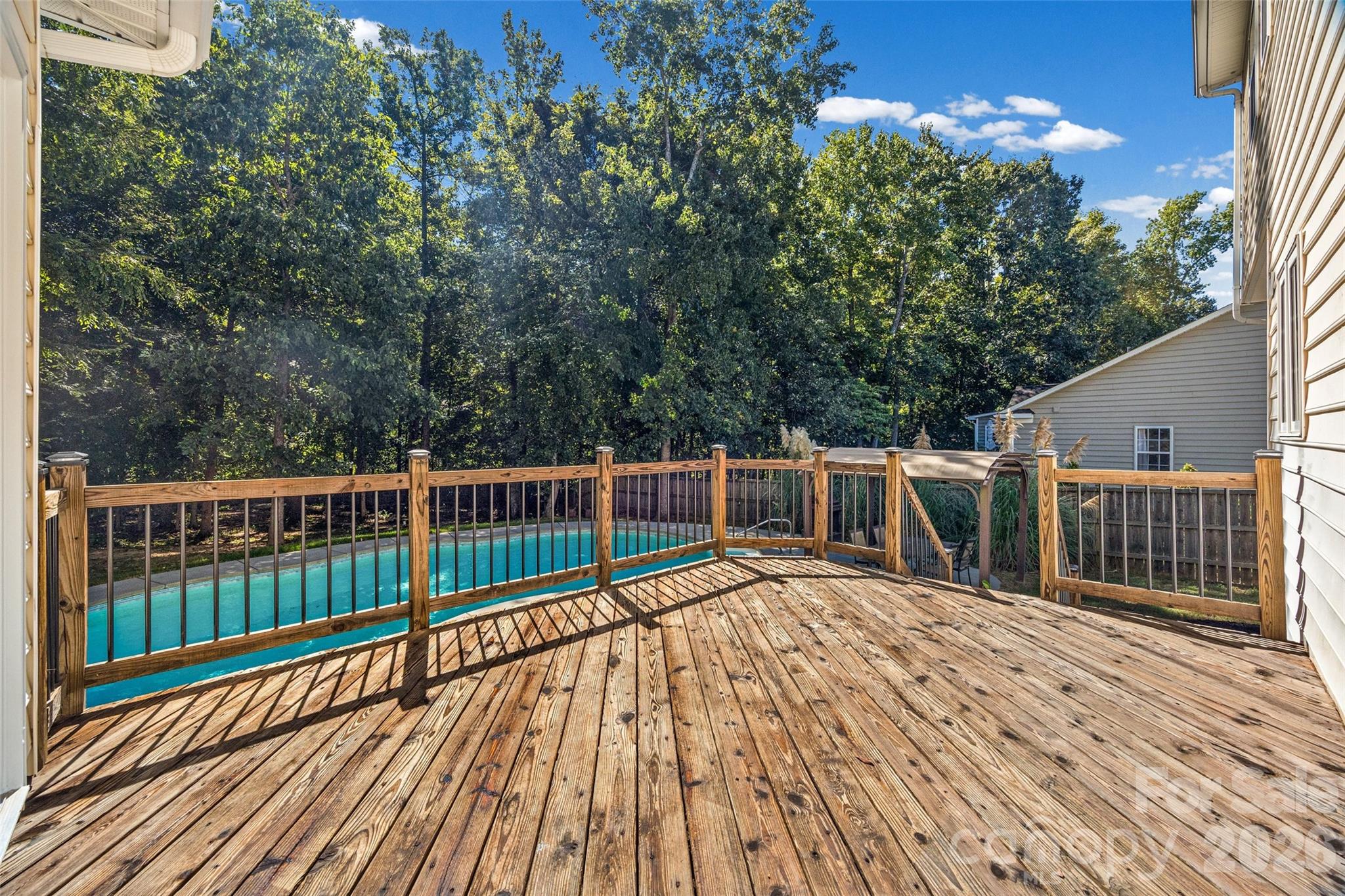 Wooden deck overlooking a swimming pool and wooded backyard.
