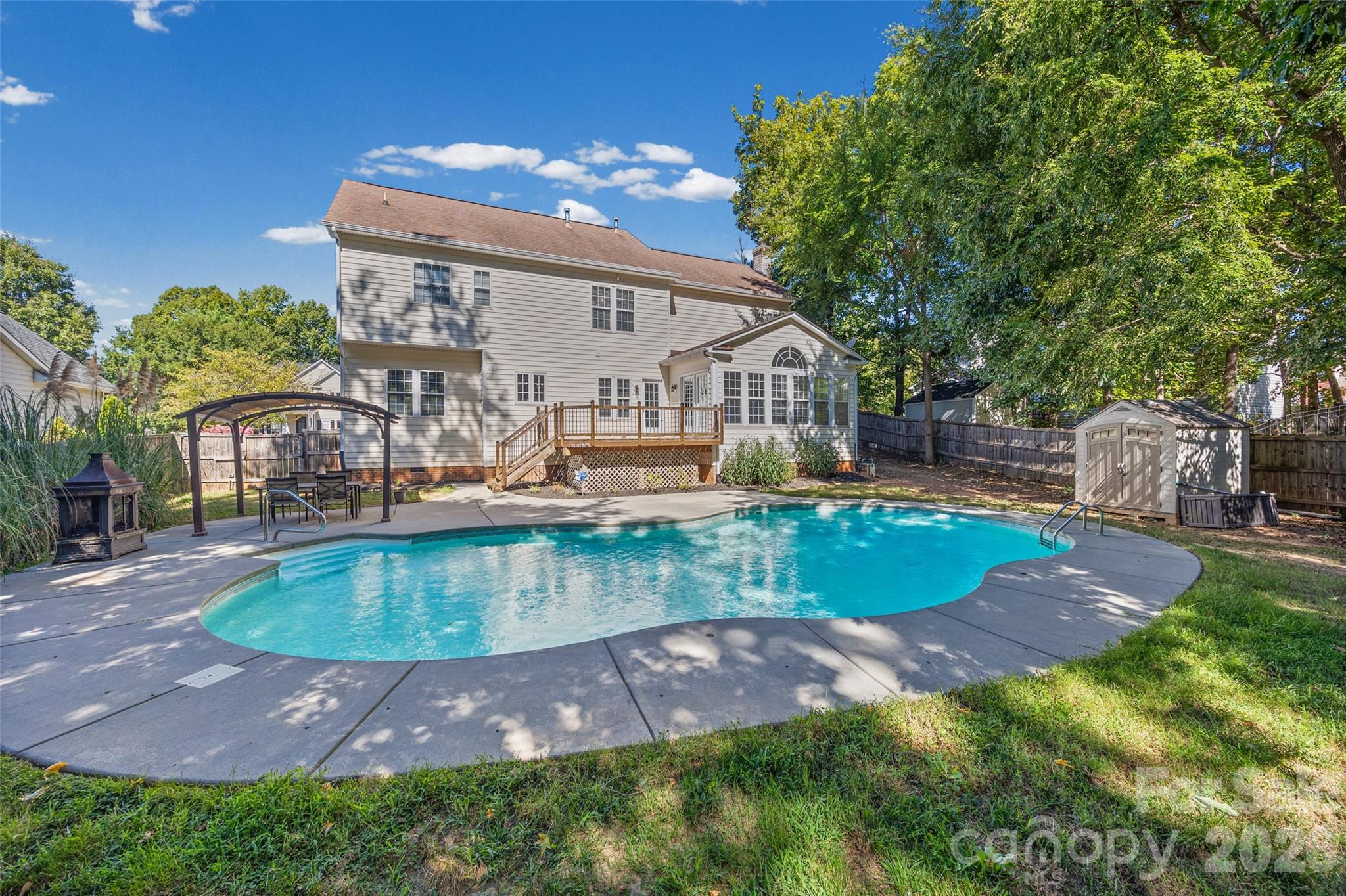 Back of a two-story home with a freeform swimming pool, raised deck, and covered patio.