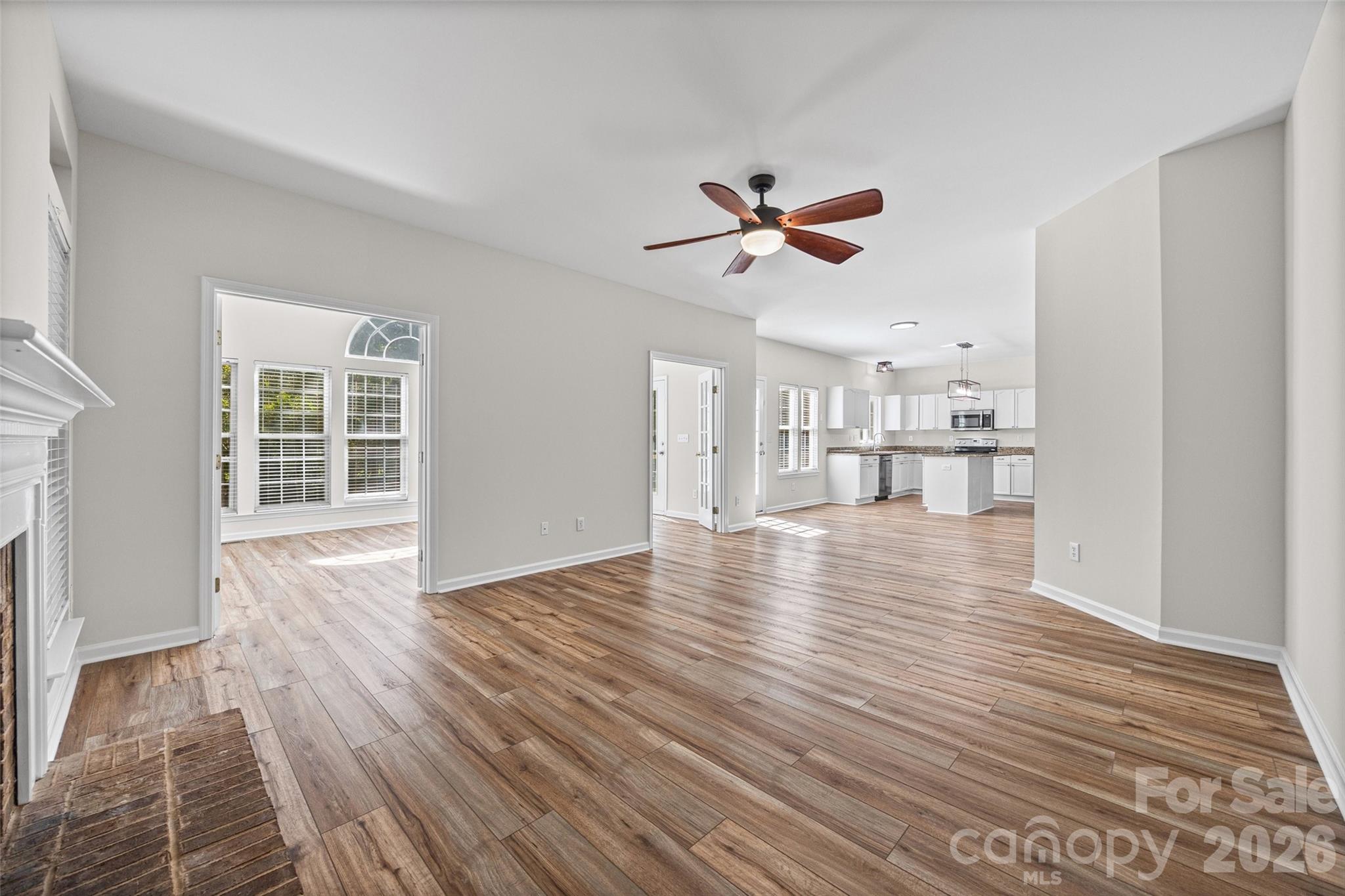 Open living area with wood-look flooring, a ceiling fan, and a kitchen with white cabinets and an island.