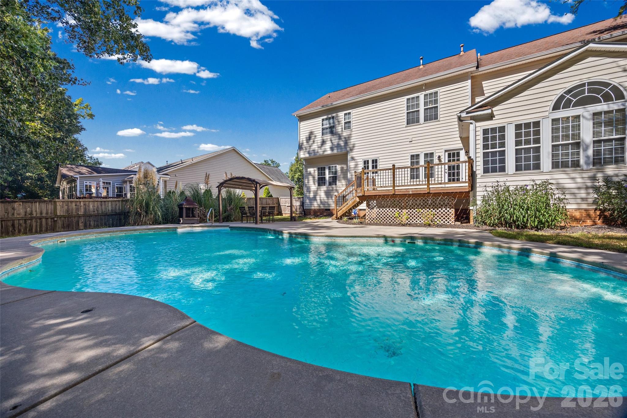 Backyard swimming pool beside a two-story home, with a raised deck and pergola.