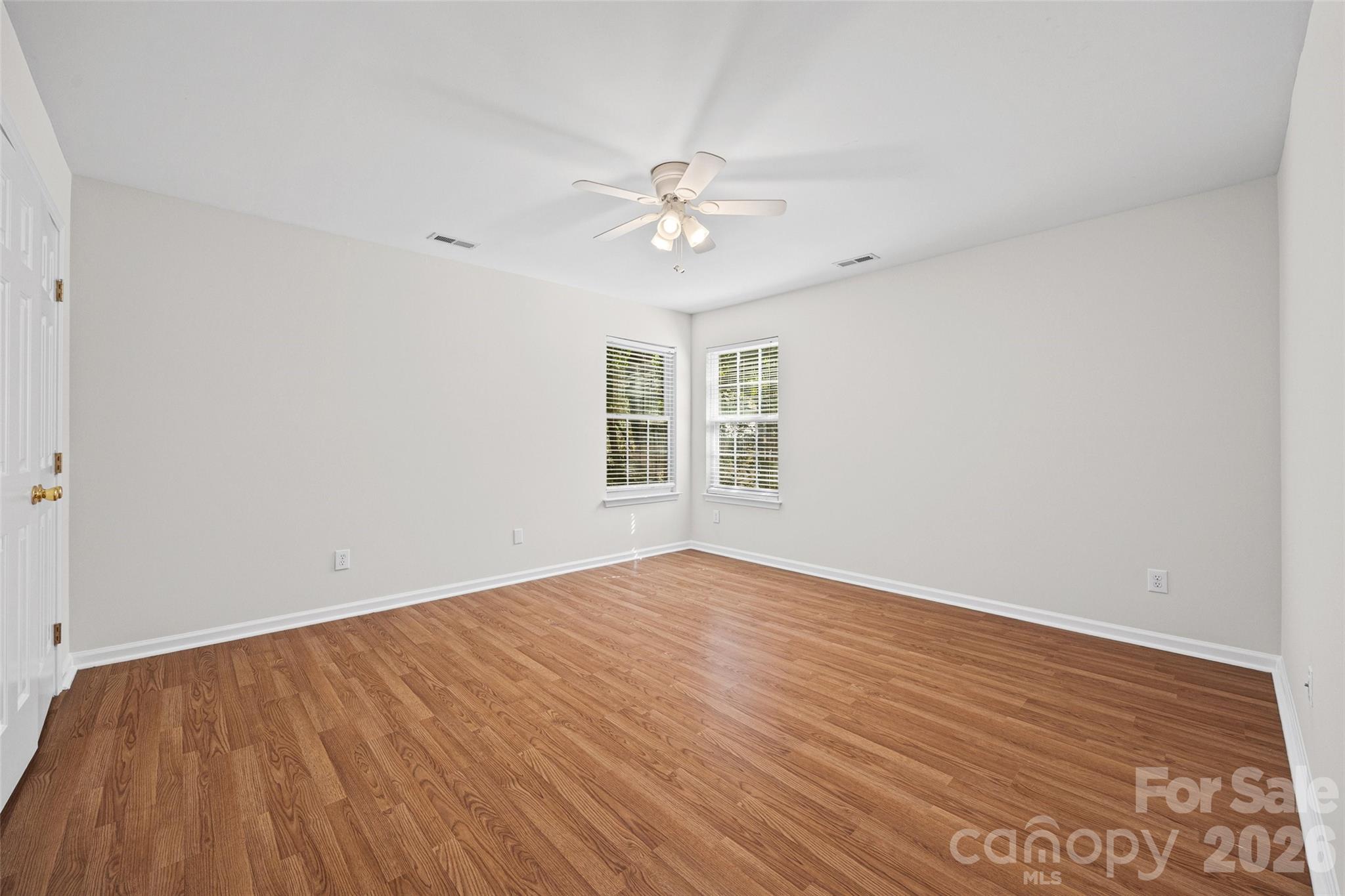 Empty bedroom with hardwood floors, two corner windows, and a ceiling fan.