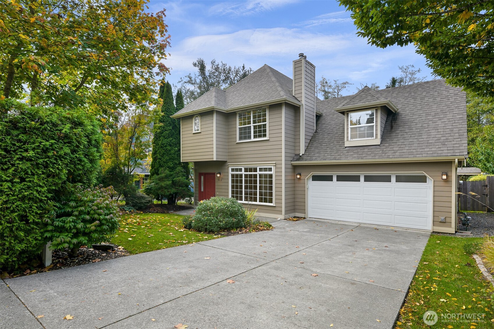 Two-story gray house with a red front door, double garage, and landscaped autumn yard.
