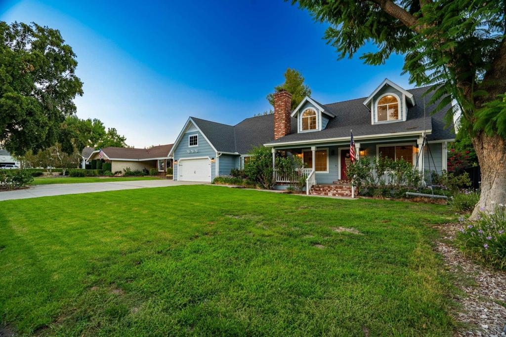 Blue house with a covered porch, arched dormer windows, attached garage, and broad front lawn.