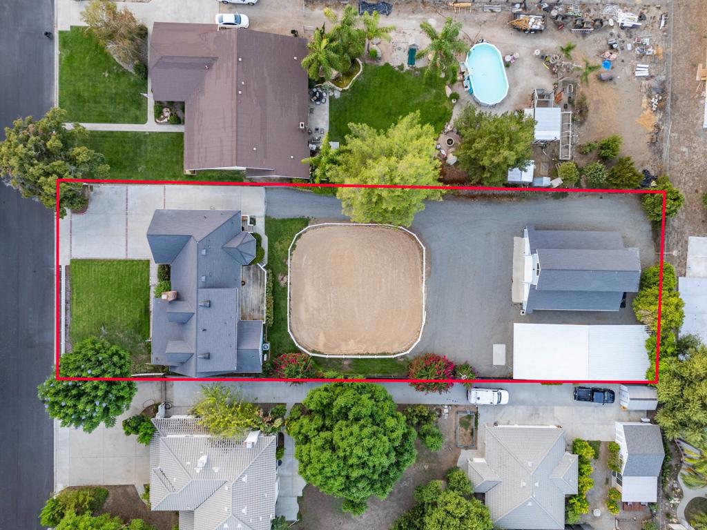 Aerial view of a house, detached outbuilding, and oval dirt arena within a red property boundary.