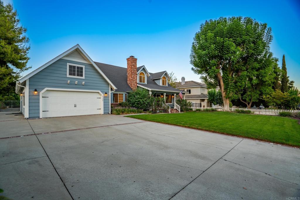 Blue-gray two-story home with a white double garage, brick chimney, and broad driveway.